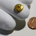 The gold quarter stater held in a gloved hand