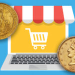A laptop with a shopping cart on the screen beside two gold coins